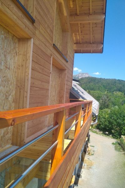 Balcon en bois ajouré avec panneau transparent, laissant passer la lumière vers l’espace en dessous