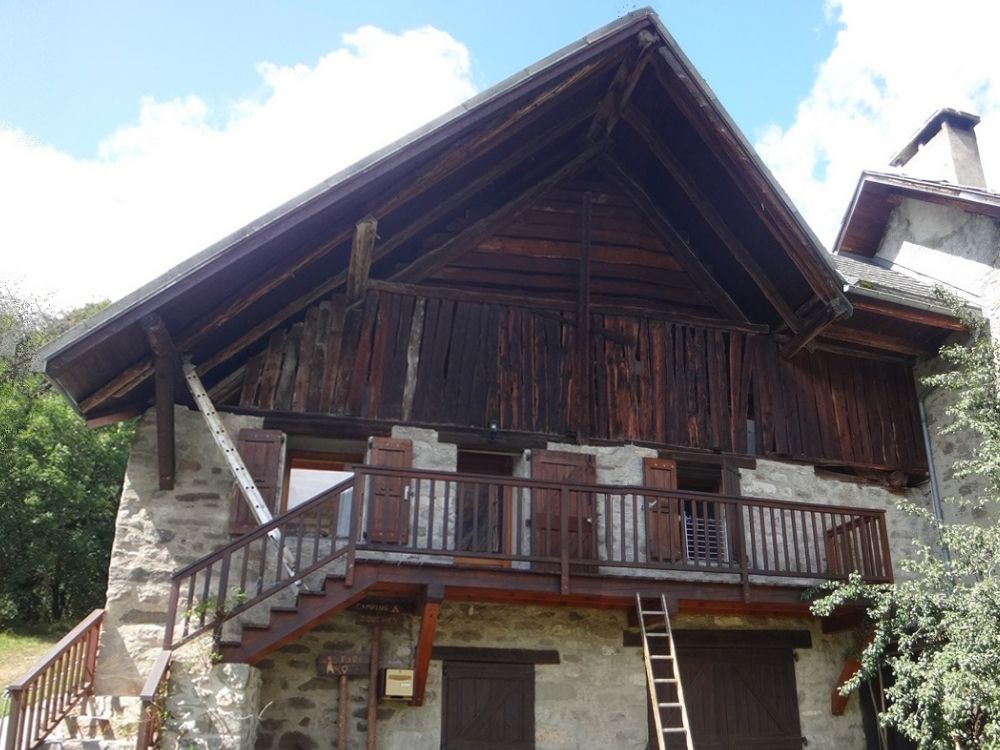 Vue d’une bâtie ancienne à Champoléon avant rénovation, avec balcon bois non sablé et structure d’origine