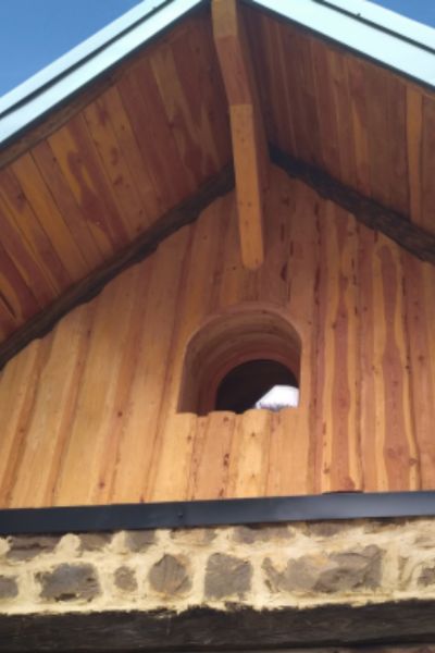 Maison en bois avec charpente apparente, façade en lames verticales et fenêtre cintrée originale